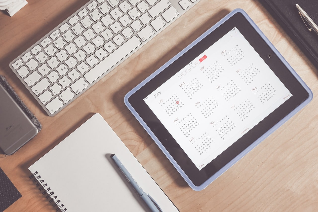 calendar application on tablet with keyboard and notebook alongside